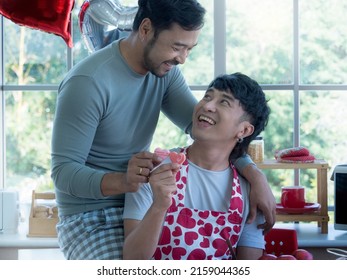 Close Up, Romantic LGBTQ Gay Couple Having A Sweet Moment, Holding Small Heart Cookies Together While Looking At Each Other With Love And Understanding In The Lovely Kitchen At Home. 