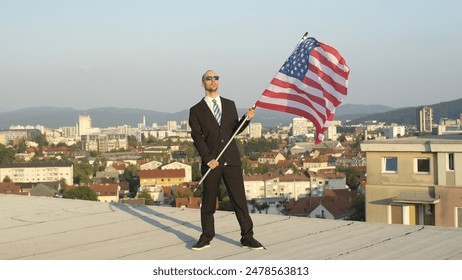 CLOSE UP: Satisfied successful businessman and patriot standing on top of tall building holding American flag proudly, celebrating success and supporting homeland, nation, culture, freedom - Powered by Shutterstock