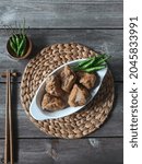 Close up, selective focus and soft blurry on hlfried tofu meatball in the white oval bowl, with green cayenne ornament at brown round wicker pedestal, flatlay style with rustic table as a background.
