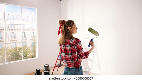 Close up. Side view of pretty joyful Caucasian woman alone painting room in new house in green color. Beautiful female renovating home painting wall using roller brush redesigning apartment