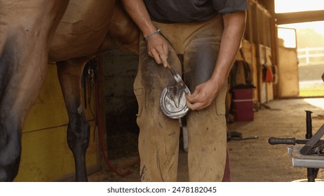 CLOSE UP: Skilled blacksmith placing metal horseshoe on horse's hoof and nailing it. Expert farrier shoeing horse, putting nails in through the insensitive hoof wall to protect sole - Powered by Shutterstock