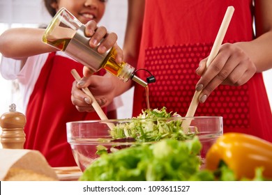 Close up. Small daughter pours olive oil into salad prepared by mother. Cooking and nutrition concepts. - Powered by Shutterstock