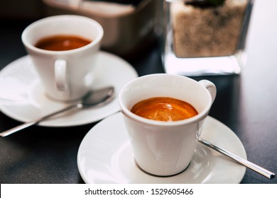 Close Up. The Small White Ceramic Mug (cup) With Italian Espresso (coffee) On A Table With A Saucer And A Metal Spoon In A Local Italian Bar (coffee Shop) In Milan, Lombardy, Italy. Beverage.