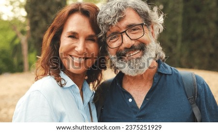 Close up, smiling older married couple looking at the camera while standing in the park hugging each other