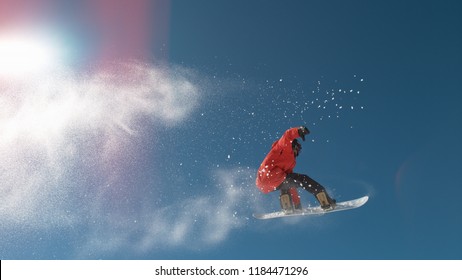 CLOSE UP: Snowboarder Jumping Big Air Kicker, Spraying Snowflakes And Flying Over Sun On Perfect Winter Day. Snowboard Jump In Snow Park. Sunbeams Shining Past Jumping Boarder In Mountains