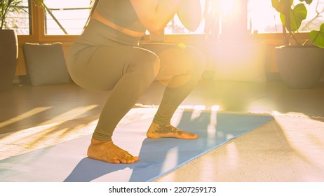 CLOSE UP: Sporty Young Woman Performing Squats At Home Workout In Golden Light. Fit Lady In Sportswear During Bodyweight Training Doing Exercises For Leg And Lower Back Muscles And Body Stability.