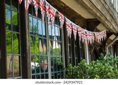 CLOSE UP: String of Union Jack flags strewn under wooden beams of an old house. Bunting English pennant as a symbol of a festive atmosphere and a patriotic pride in historic town during celebration.