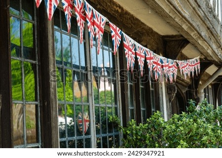 CLOSE UP: String of Union Jack flags strewn under wooden beams of an old house. Bunting English pennant as a symbol of a festive atmosphere and a patriotic pride in historic town during celebration.