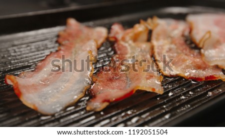 CLOSE UP: Strips af bacon on a black grill
