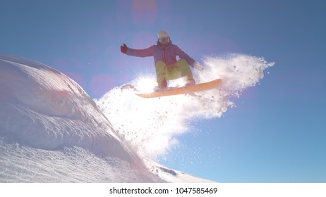 CLOSE UP, SUN FLARE: Young Snowboarder Performs Epic Jump On Perfect Powder Snow Covered Mountain Slope. Active Man On Winter Vacation Takes Off High In The Air On His Cool Snowboard. Adrenaline Hobby