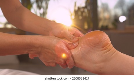 CLOSE UP: Sunrays shine through massaging hands while performing reflexotherapy. Reflexology therapy for stress ease and helping body work better. Relaxing wellness treatment at the end of the day.