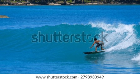 CLOSE UP: Surfer makes a bottom turn and sprays while riding perfect glassy wave. Riding perfect breaking waves in the embrace of wild natural beauty of a remote surfing paradise in tropical Indonesia