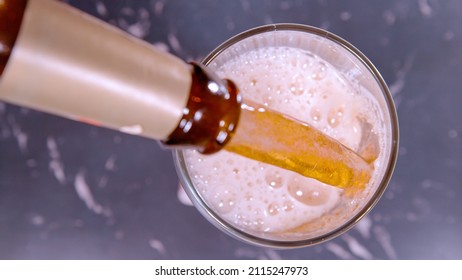 CLOSE UP, TOP DOWN, DOF: Ice Cold IPA Beer Gets Poured Out Of A Brown Vintage Bottle And Into A Glass. Frothing Pale Ale Gets Poured From A Retro Bottle. Pouring Refreshing Light Beer Into A Mug.