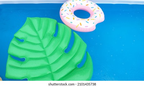 CLOSE UP, TOP DOWN: Late summer rain begins pouring down on an inflatable leaf and donut floating around an empty pool. Raindrops falling into the pool create ripples on the surface of the water.