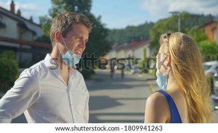 CLOSE UP: Two irresponsible young friends talk in the middle of the suburban street without having their masks on. Young woman talks to man without social distancing and wearing their protective masks