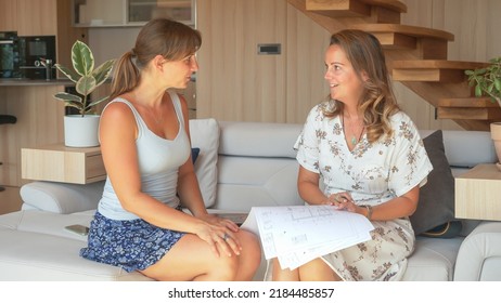 CLOSE UP: Two Young Women Holding And Looking Architectural House Building Plans For Efficient Furniture Arrangement. Onsite Consultation Between Investor And Interior Design Architect In Living Room.