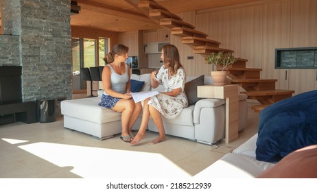 CLOSE UP: Two Young Women Sitting On A Sofa And Consulting Interior House Design. Home Owner And Design Expert Discussing House Building Plans To Efficiently Organize And Arrange Home Living Space