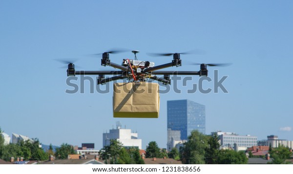 CLOSE UP: UAV drone delivery delivering big brown\
post package into urban\
city