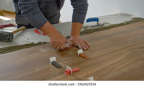 CLOSE UP: Unrecognizable Contractor Places Plastic Wedges To Seal Laid Tiles And Leave Them To Dry. Tiler Fastens The Laid Tiles To Leave The Adhesive Mortar To Dry Overnight. Craftsman At Work.