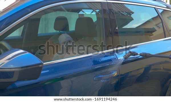 CLOSE UP: Unrecognizable virologist sprays the\
car\'s door handle with antiviral spray. Sanitation specialist in a\
white hazmat sprays and disinfects the car and streets during the\
covid-19 pandemic.