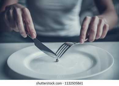 Close Up. Woman Eating One Pea With Fork And Knife. Diet Concept. Weight Loss Problem. Starving Young Woman. One Pea On White Plate. Hungry Woman Lying On White Sofa. Healthy Lifestyle Concept.