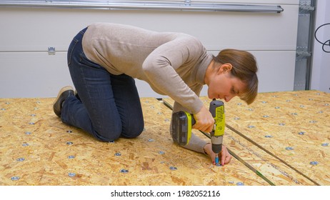 CLOSE UP: Woman Fastens Metal Washers Onto A Plywood Board With A Power Drill. Close Up Shot Of A Female Worker Screwing Thin Metal Discs In Place On A Plywood Panel. Home Improvement In Progress.