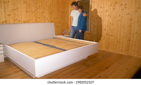 CLOSE UP: Young Caucasian Couple Hugs After Assembling Their King Sized Bed In The Wooden Bedroom. Man And Woman Mount Bunkie Boards Onto The Bed Frame Of A Large Bed In Their Brand New Bedroom.