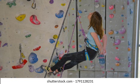 CLOSE UP: Young Caucasian girl climbing indoors chalks up before continuing her ascent. Teenage rock climber reaches in her pouch to apply some magnesium powder on her hands to improve her grip. - Powered by Shutterstock