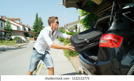 CLOSE UP: Young Man Is Happy To Get All The Travel Bags In The Trunk Of His Car While Packing For His Awesome Journey. Funny Shot Of Carefree Guy Living In The Suburbia Tossing Luggage In Black Car.