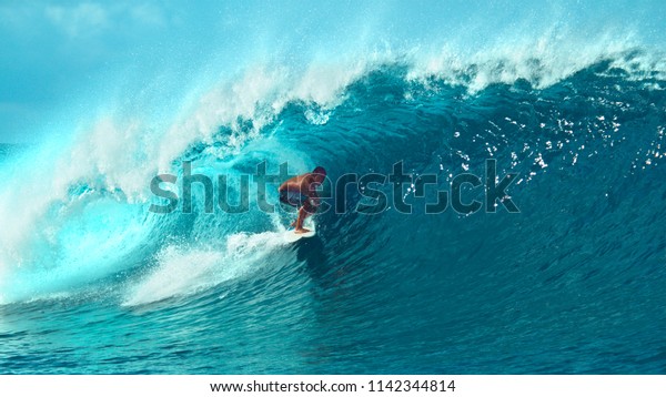 CLOSE UP: Young pro surfer surfs a big barrel\
wave in popular surf spot in breathtaking Tahiti. Awesome view of a\
extreme surfboarder riding epic blue waves in the hot summer sun of\
French Polynesia.