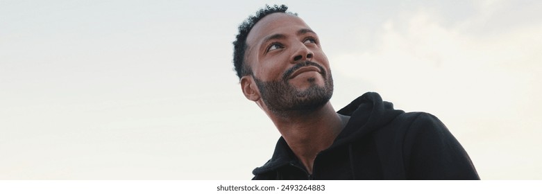 Close up, young smiling bearded male athlete dressed in hoodie uses cellphone after training while sitting on the embankment - Powered by Shutterstock