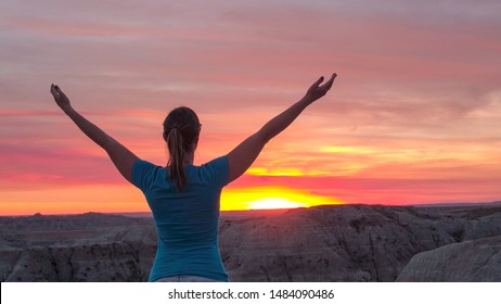 CLOSE UP: Young woman relaxing and raising her arms slowly towards the pink sky at stunning autumn sunset. Happy hiker peacefully rising hands up and enjoying the moment at red sunrise
