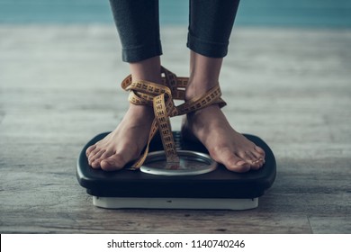 Close Up. Young Woman Standing On Weigher On Floor. Diet Concept. Weight Loss Problem. Starving Young Woman. Tailors Centimeter. Hungry Woman. Healthy Lifestyle Concept. Wooden Floor.