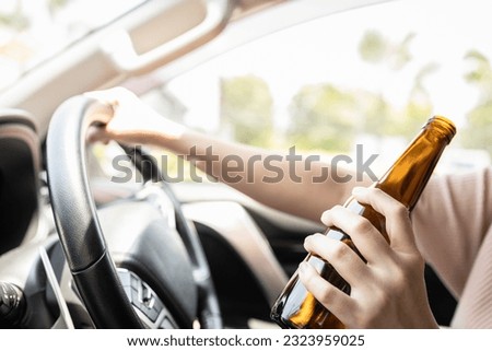 Close up,Hand of drunk woman holding bottle of beer,asian female driver drinking alcohol while driving motor vehicle,bad behavior,losing control,road accident problems,concept of Don't drink and drive