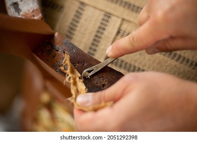 A close up of upholsterer's hands removing antique upholstery nails. Restoration of an antique chair. - Shutterstock ID 2051292398
