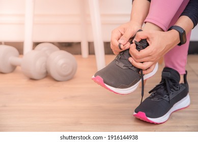 Close Upp Of Young Asian Muslim Woman In Pink Workout Dress Tying Her Shoelaces In Her Living Room, Preparing For Workout, Indoor Home Exercise Concept