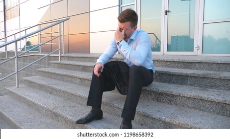 Close up of upset sad manager sitting on stairs near office building and crying. Desperate young businessman got a very bad news on phone and feeling despair outdoor. Concept of financial crisis.