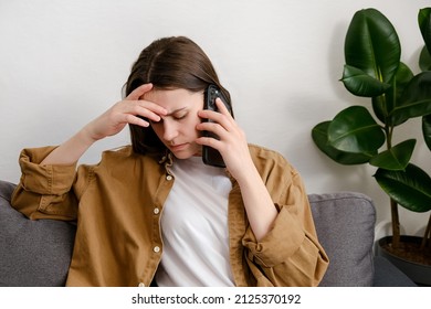 Close Up Of Upset Sad Young Woman 20s Old Years Speaks On Smartphone Sitting On Sofa In Living Room At Home, Gets Bad News. Adult Tired Millennial Lady Talking On Phone Sit Alone On Grey Couch