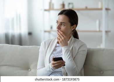 Close up upset unhappy young woman holding smartphone, thinking about problems, stressed frustrated girl received bad news in email or message, waiting for boyfriend call, sitting on couch alone - Shutterstock ID 1873193875