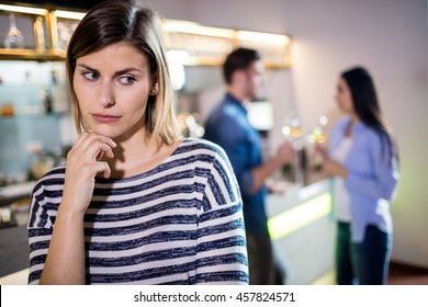 Close up of upset woman with hand on chin while boyfriend talking with female friend in background
