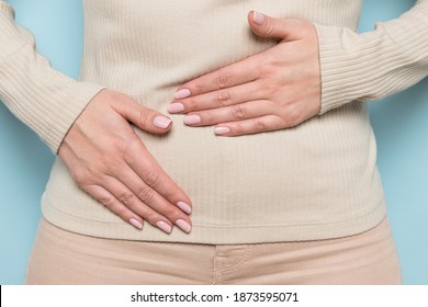 Close up of upset woman hold belly suffer from abdomen ache, female feel pain hurt in stomach abdominal gastritis, pancreatitis, food poisoning, appendicitis symptom, standing over blue wall.