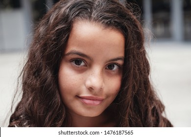 Close up urban lifestyle portrait of a confident, gorgeous mixed race child face, head shot of multiethnic tween preteen teen girl with beautiful curly hair, smiling at camera, youth day