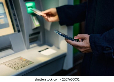Close up of using cell phone while inserting credit card in ATM machine. 