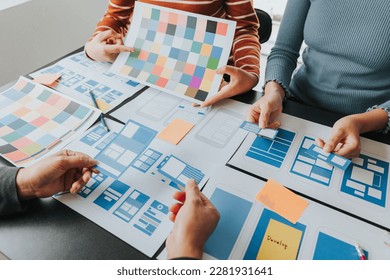 Close up ux developer and ui designer brainstorming about mobile app interface wireframe design on table with customer breif and color code at modern office.Creative digital development agency