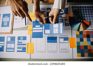 Close up ux developer and ui designer brainstorming about mobile app interface wireframe design on table with customer breif and color code at modern office.Creative digital development agency