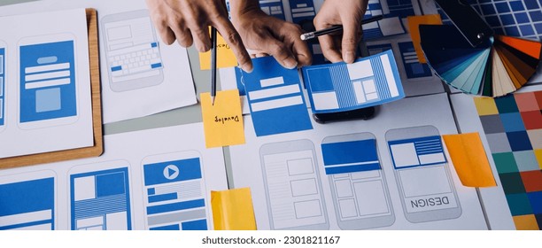 Close up ux developer and ui designer brainstorming about mobile app interface wireframe design on table with customer breif and color code at modern office.Creative digital development agency