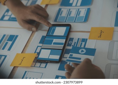 Close up ux developer and ui designer brainstorming about mobile app interface wireframe design on table with customer breif and color code at modern office.Creative digital development agency