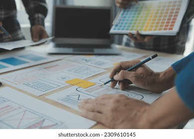 Close up ux developer and ui designer brainstorming about mobile app interface wireframe design on table with customer breif and color code at modern office.Creative digital development agency