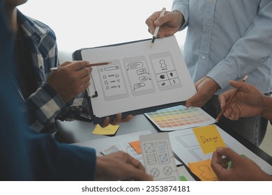 Close up ux developer and ui designer brainstorming about mobile app interface wireframe design on table with customer breif and color code at modern office.Creative digital development agency