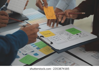 Close up ux developer and ui designer brainstorming about mobile app interface wireframe design on table with customer breif and color code at modern office.Creative digital development agency